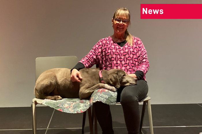 zwei Stühle nebeneinander. Auf dem rechten Stuhl sitzt Jacqueline Schaufelberger. Ihr Hund Ludwig liegt quer über dem linken Stuhl und über den Knien von Jacqueline Schaufelberger