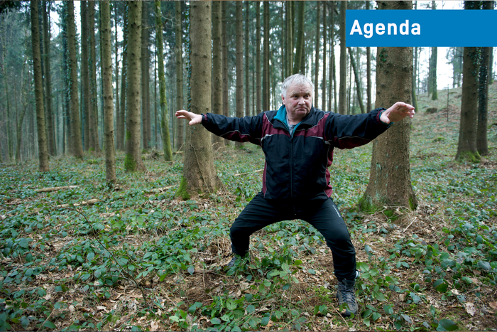 Ein älterer Herr im altmodischen, zweiteiligen Trainingsanzug steht mitten im Wald und macht eine Karate-Pose