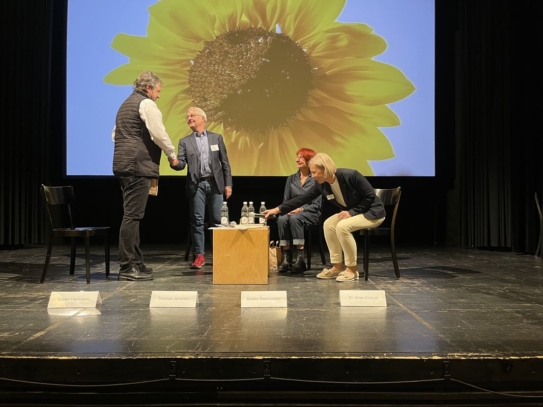 Foto der Podiumsdiskussion mit Sonnenblume im Hintergrund